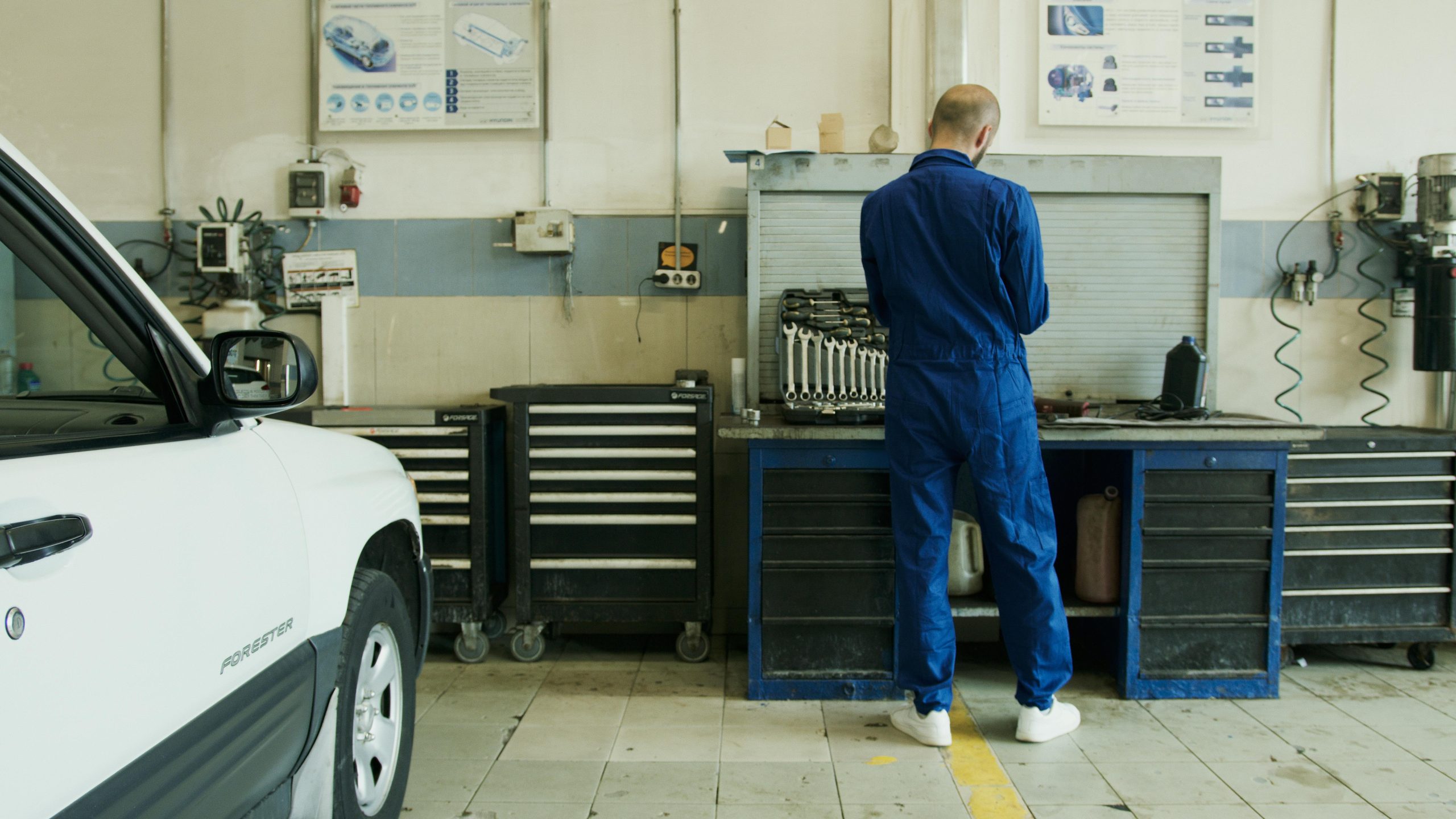 auto mechanic wearing a blue overall and a white car in an auto repair shop
